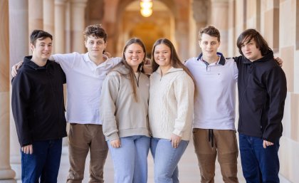 a group of six people stand in a corridor with their arms around each other